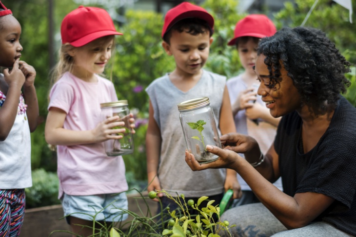 A group of children looking at a teacher holding a plant