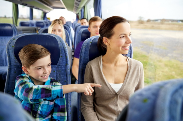 Child sits next to parent on a bus and points out the window