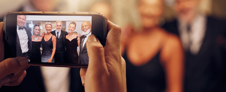 a hand holding a camera that is taking photos of well dressed people