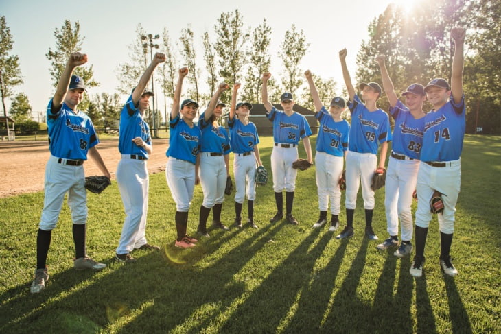 A baseball team stands in a line with fists in the air smiling