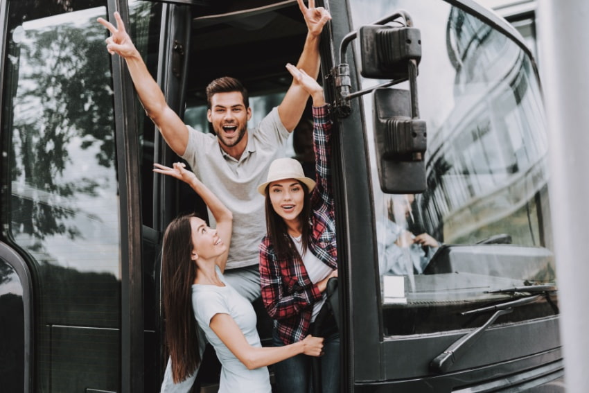 Three people stand in an open charter bus door and smile